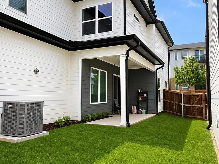 Rear exterior showcasing a covered patio, expansive green lawn, and privacy fencing