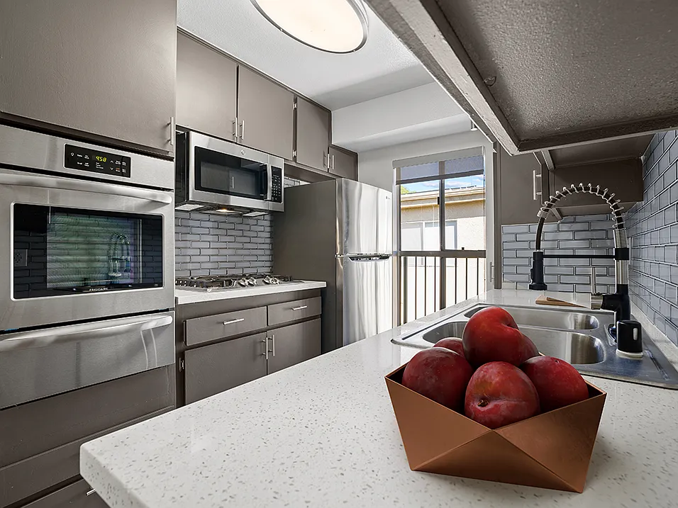Blue tiled kitchen with stainless steel oven, microwave, fridge, and fixtures.