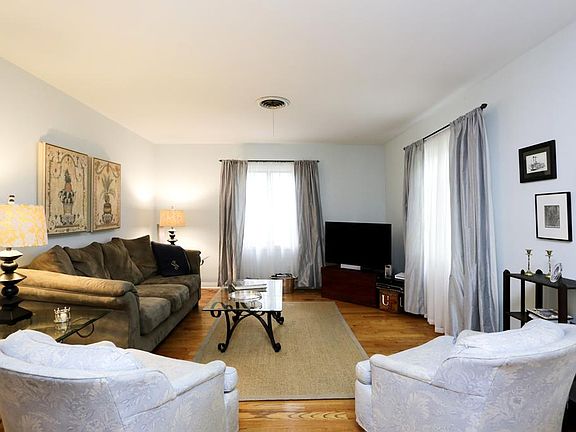 Large living room with hardwood flooring, a wall of built-ins, windows on the East and North sides, 