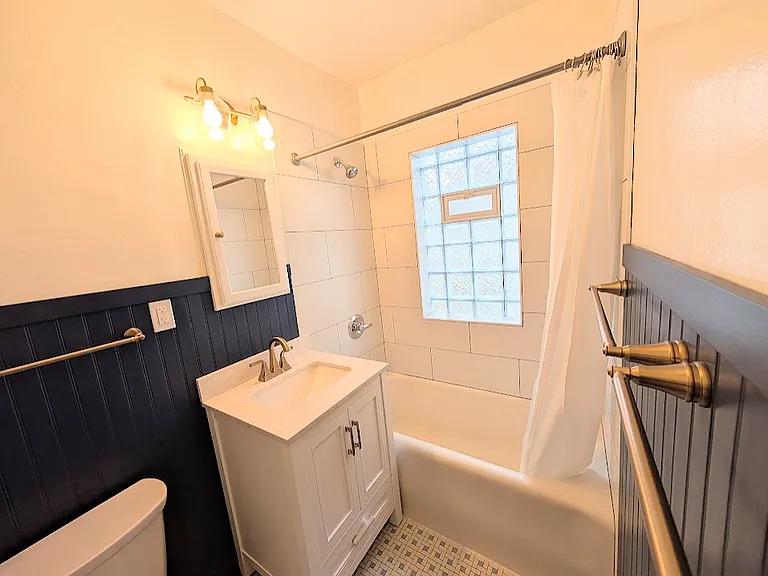 Remodeled bathroom. New security glass window with vent, new shower tile and fixtures, new vanity, new toilet, new champagne gold accents