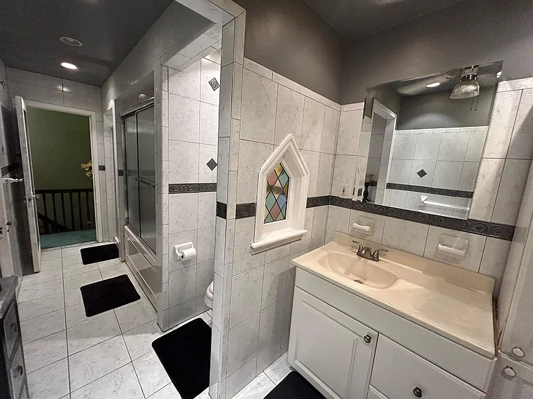 Spacious tiled bathroom with a tub/shower combo, large vanity, and decorative accent tile plus a unique stained-glass window.