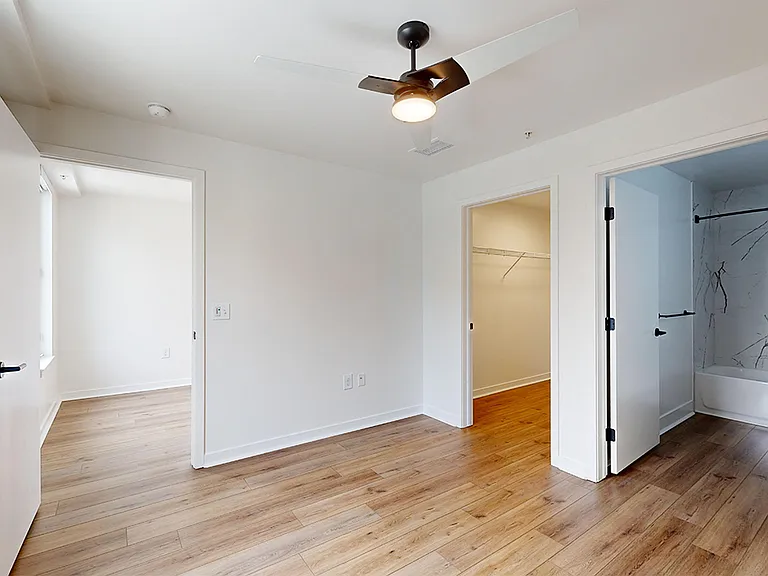 Spacious apartment bedroom with large closet, attached bathroom and wood-style flooring.