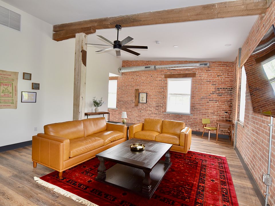 The living room features an open layout with optimal seating throughout, a desk/work space and a smart TV. The room features ceiling spotlights that are dimmable (its a whole mood) and a ceiling fan.