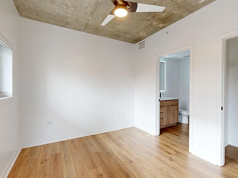 Spacious apartment bedroom with large closet, attached bathroom and wood-style flooring.