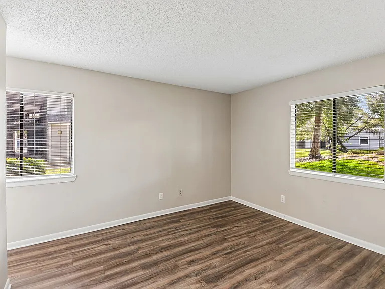 Bright room with stylish wood floors and large windows offering scenic views of lush greenery.