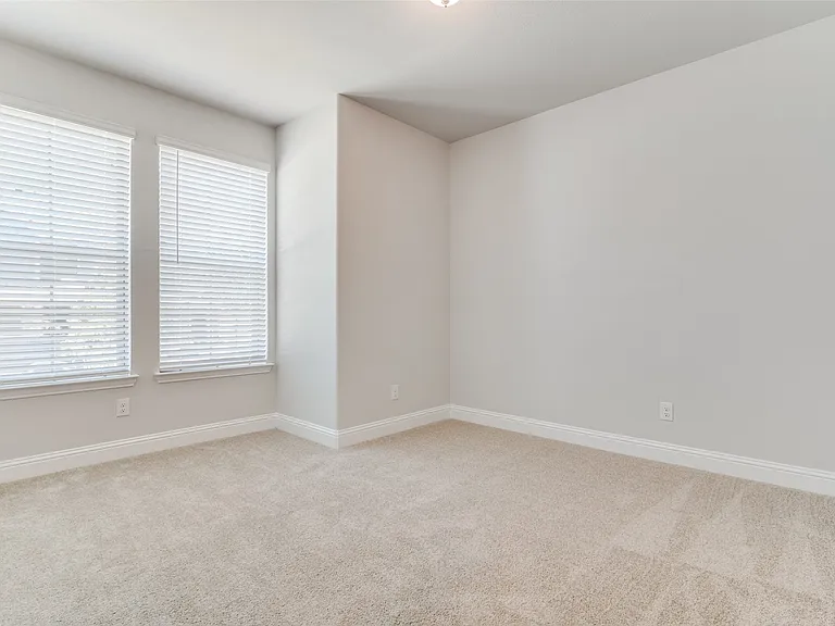Neutral-toned carpeted room featuring two prominent windows with horizontal blinds
