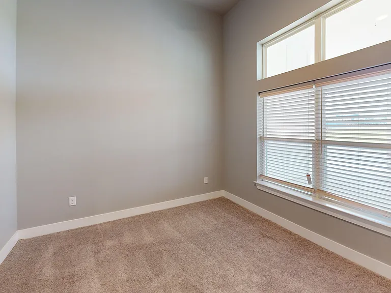 The Bellview's one bedroom features a large window and carpeted flooring. The Bellview's one bedroom features a large window and carpeted flooring.