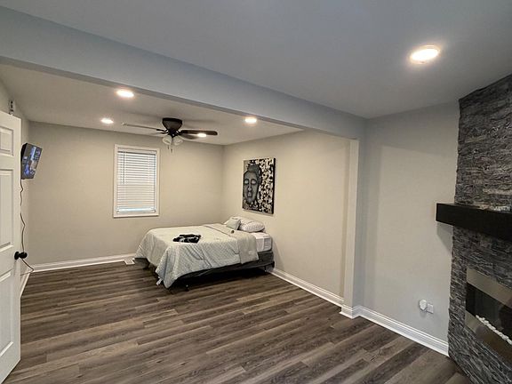 Spacious bedroom with plank flooring, overhead lighting, ceiling fan, and a window with blinds for privacy.