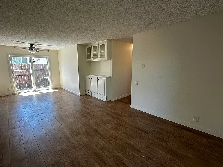 Photo from corner of Living Room facing the Dining Room with Ceiling Fan, Access to Small Private Patio, Built in Vanity and hallway on the right. Sliding Door to Large Balcony is behind the camera angle