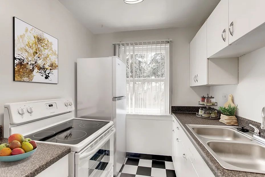 Kitchen with stove fridge sink cabinets and black and white tile floor with window in back