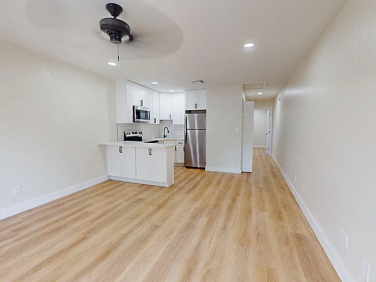 Modern open-plan living area with elegant wood flooring, featuring a sleek kitchen with stainless steel appliances and minimalist white cabinetry.