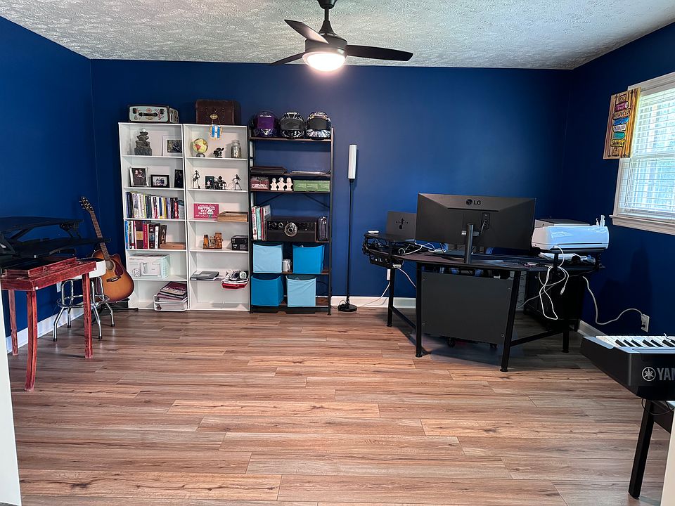 Office room with a ceiling fan and two windows on the right side gives you plenty of light and is an open floor concept into the second living room or playroom for kids. You could work from this room and see your kids play right in the other room!