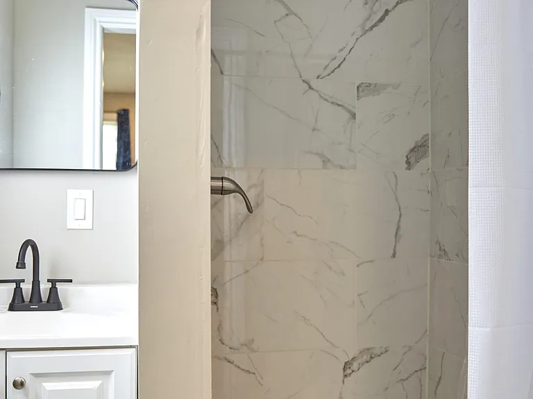 Full bath with tiled tub/shower surround, updated fixtures, and a vanity with mirror for everyday storage and prep.