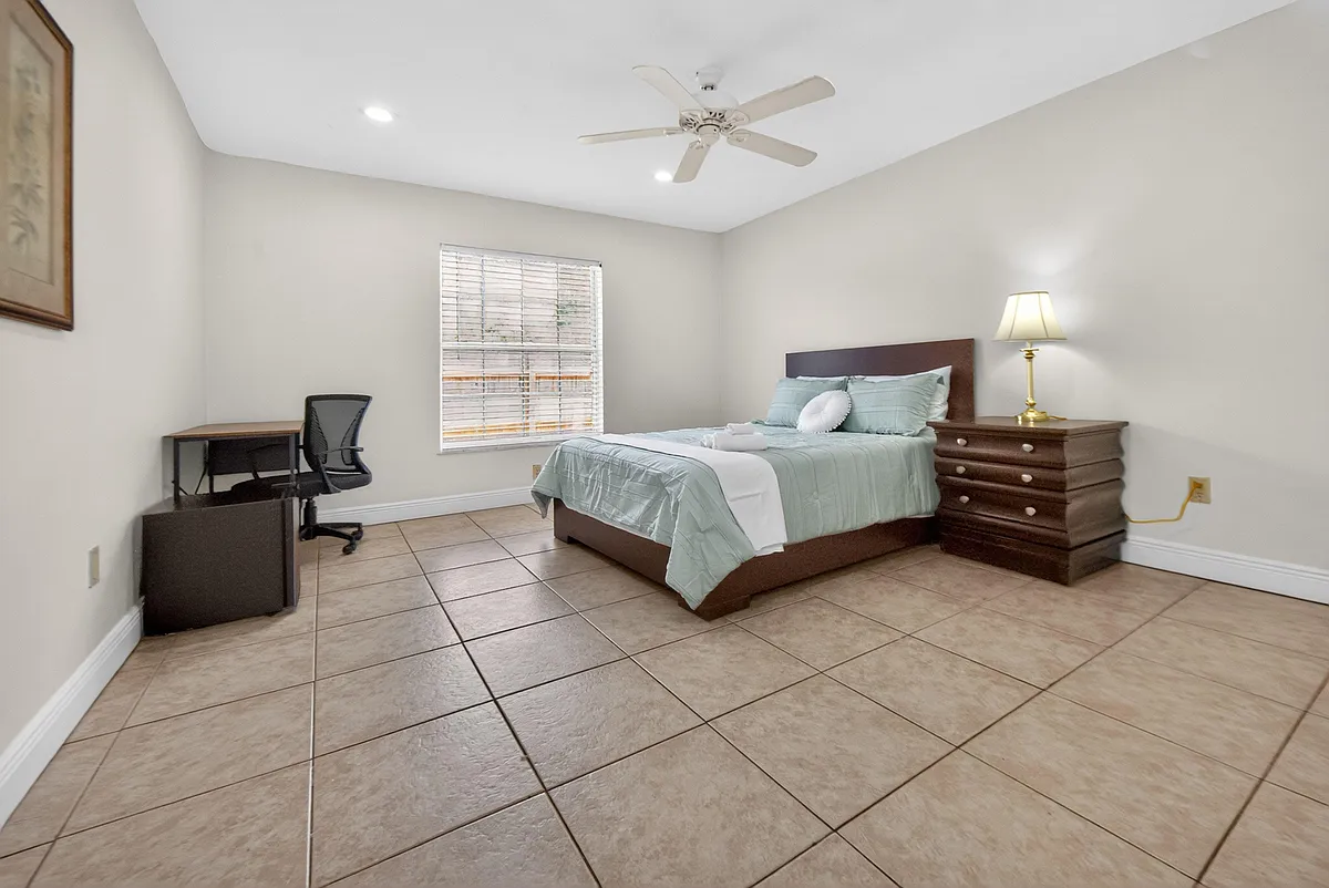 Spacious bedroom with tile flooring, ceiling fan, window blinds, and a dedicated desk area plus dresser storage. - SW 43rd Terrace Rd