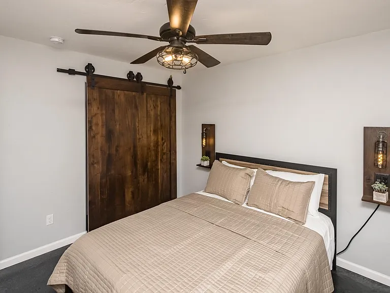 Private guest bedroom featuring custom barn-style closet doors, modern ceiling fan, and sleek flooring.