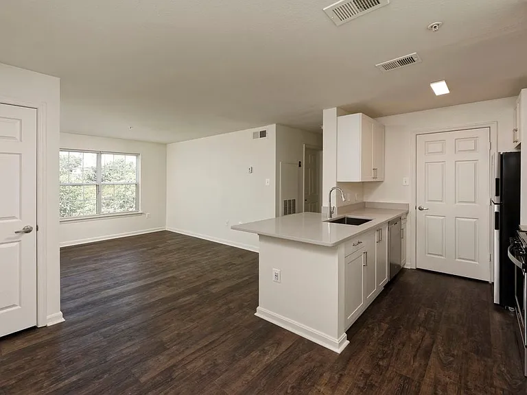 Renovated Package II kitchen and living areas with light grey quartz countertops, white cabinetry, stainless steel appliances, and hard surface flooring