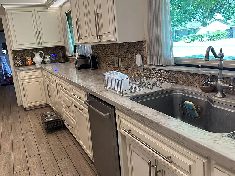 Spacious kitchen with ample shaker cabinetry, long prep counters, and a deep sink set beneath a large window.