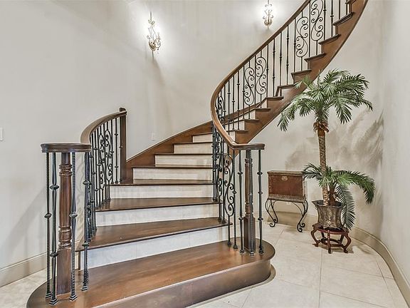 An impressive sweeping curved staircase with wrought iron spindles oak trends and Tile floors makes a statement in this two story grand foyer.