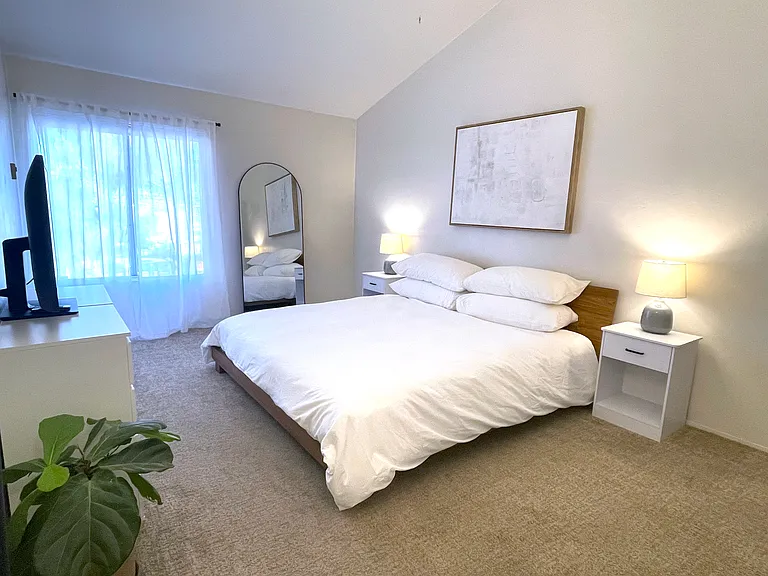 Spacious primary bedroom with king bed, dresser, and TV