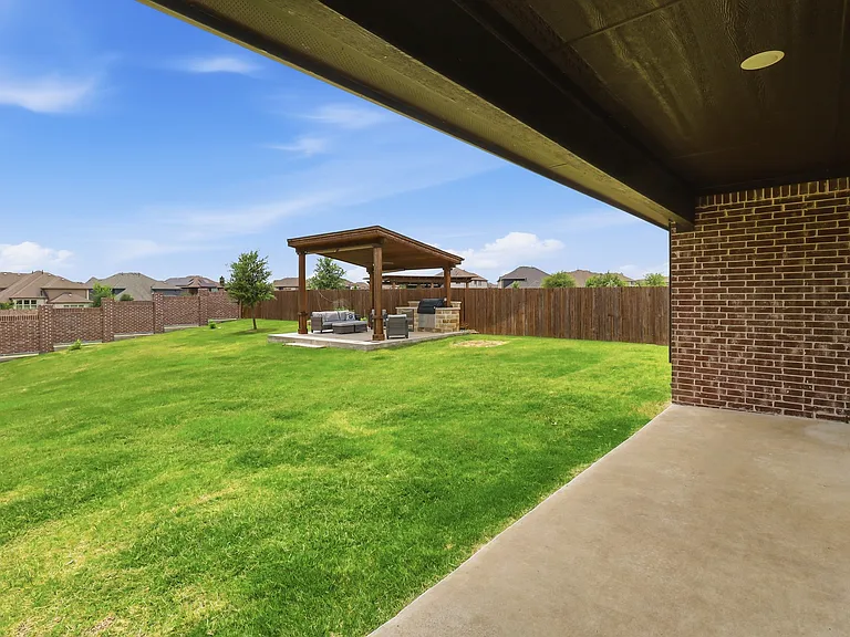 Covered Backyard Patio featuring a lush lawn wooden privacy fencing, and a brick exterior