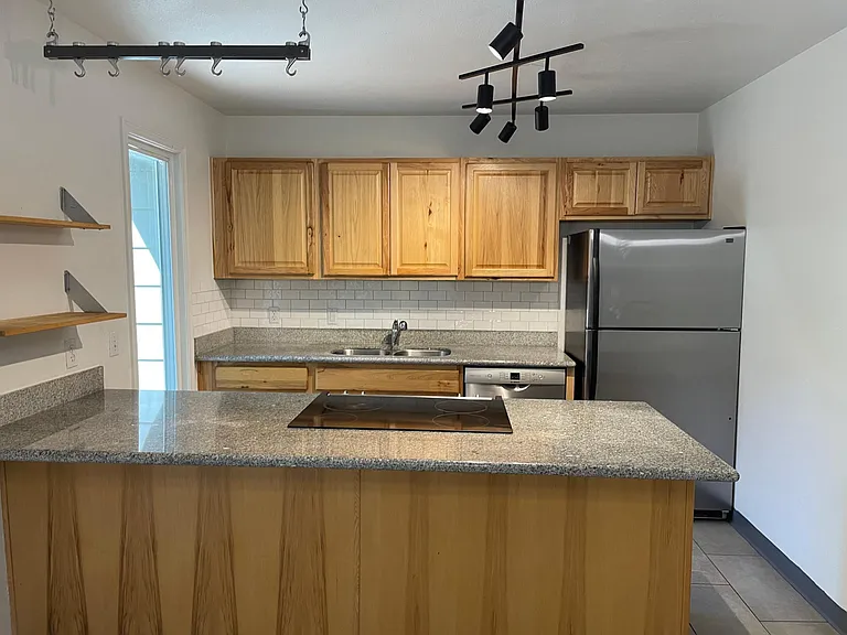 Kitchen with stainless steel appliances and island with large granite countertop able to accommodate barstools.
