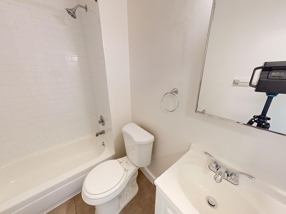 Compact bathroom with a bathtub and shower, a toilet, and a sink with a mirror. The space is bright and clean, with floor tiles.