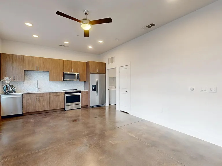 Apartment kitchen with stainless steel appliances, dining and living room with polished concrete flooring.