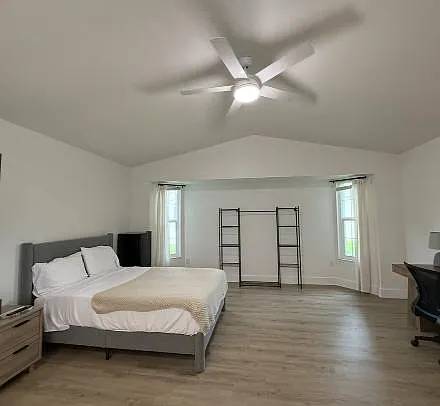 Spacious bedroom with a ceiling fan, wood-style flooring, and two windows for natural light, plus room for a work area.