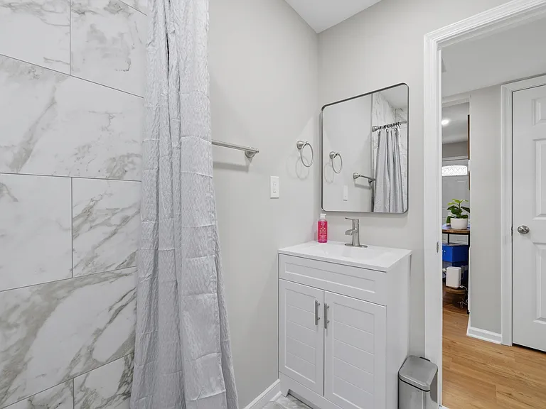 Updated bath with marble-look tiled shower, vanity with storage, and a large mirror for everyday convenience.