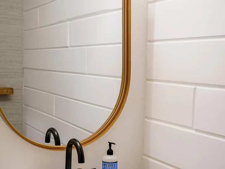 Downstairs renovated bathroom with a shiplap feature wall, matte black hardware, and gold oval mirror.
