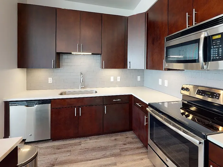 Apartment kitchen with stainless steel appliances, quartz countertops and wood-style flooring.
