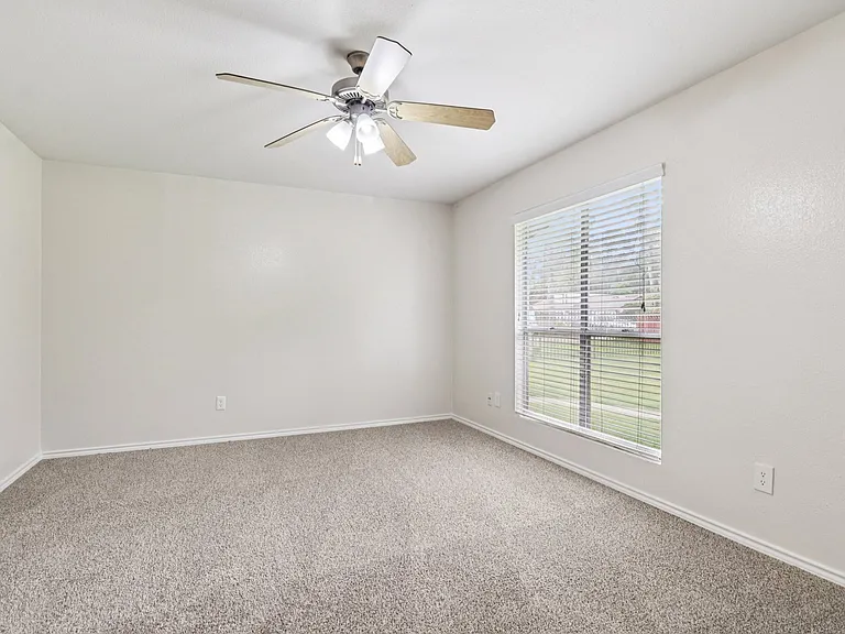 Bright and airy bedroom with plush carpeting, large window with blinds, and a ceiling fan, offering a welcoming and comfortable space. Bright and airy bedroom with plush carpeting, large window with blinds, and a ceiling fan, offering a welcoming and comf