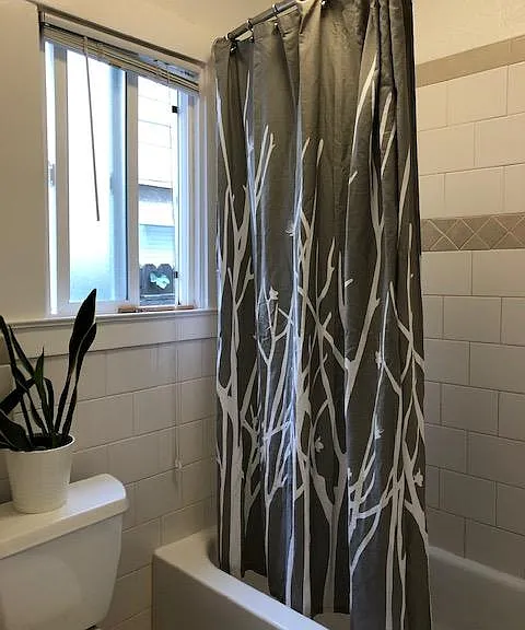 Spacious bathroom with bath/shower combination with tile shower surround,large bath vanity, tile flooring, window for natural light.