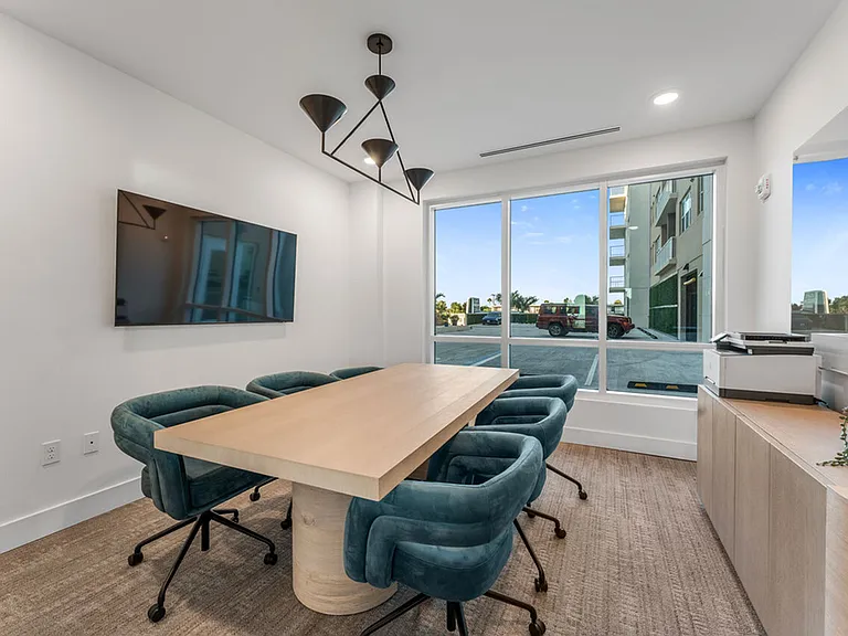 Modern conference room with a sleek wooden table, six plush teal chairs, and a large window offering a bright, spacious atmosphere.