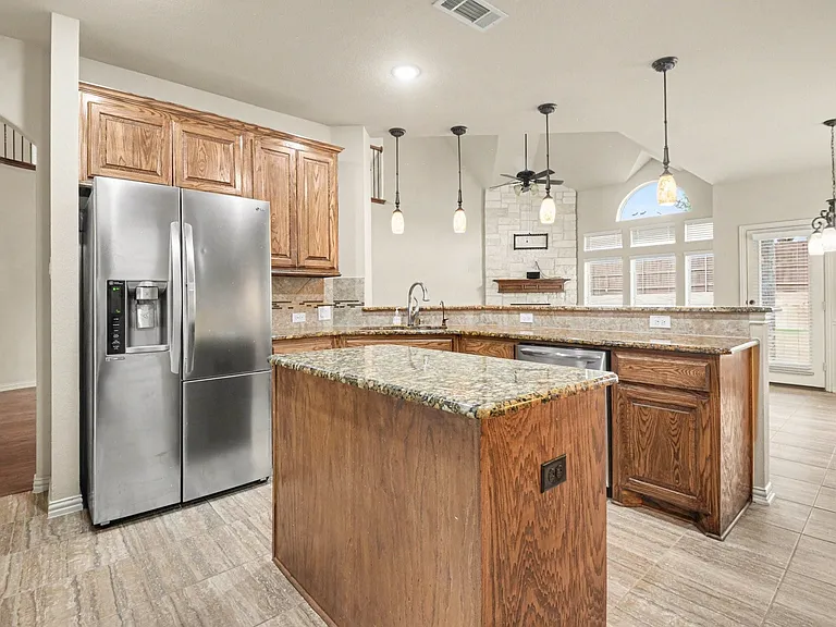 Kitchen featuring wood cabinetry, granite countertops, tile flooring, a stainless steel refrigerator, and pendant lighting