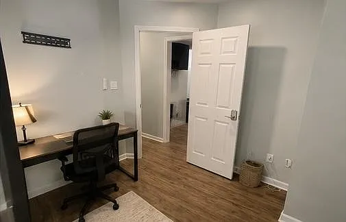 Flexible room with a dedicated desk workspace, wood-style flooring, and convenient access to the hall and adjacent areas.