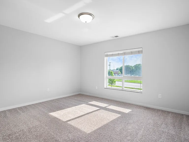 Spacious, sunlit bedroom with large window and plush carpet creating a warm and inviting atmosphere. Spacious, sunlit bedroom with large window and plush carpet creating a warm and inviting atmosphere.