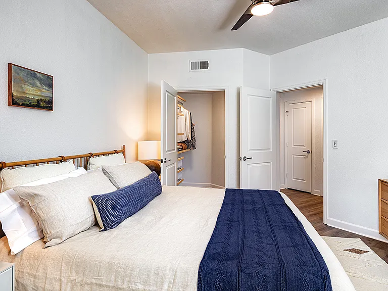 A bedroom with a bed, a ceiling fan, and open doors revealing a walk-in closet and another room.