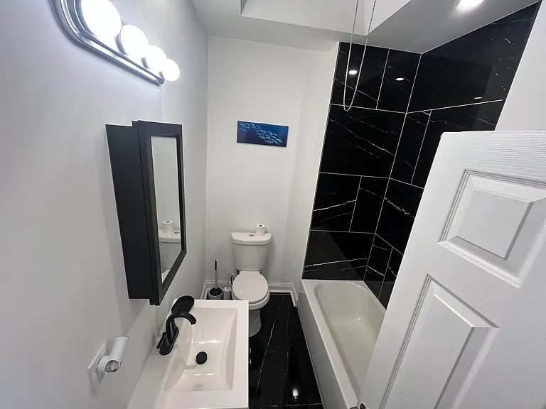 Bathroom with a tub/shower combo, bold tile surround, and a vanity with mirrored storage and updated fixtures.