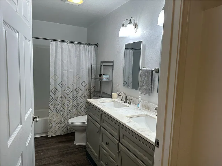 Bathroom featuring a dual vanity with a light-toned countertop, wood-finish flooring, a white porcelain toilet, and a combined tub and shower