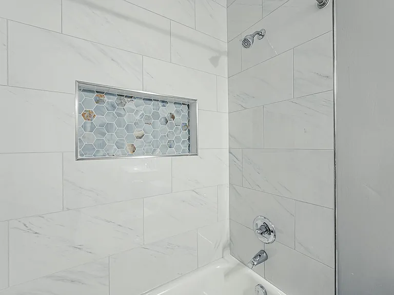 Tub/shower combo with large-format tile surround, chrome fixtures, and a built-in niche with decorative mosaic accent.