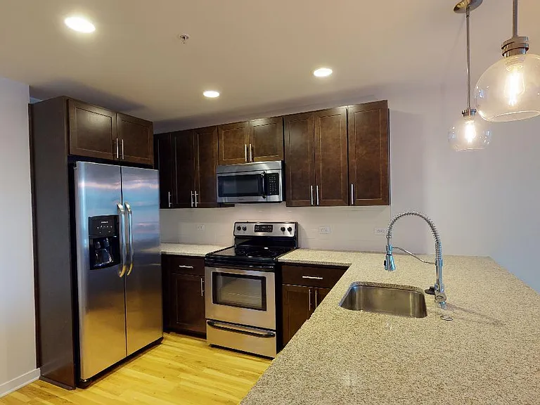 Apartment kitchen with stainless steel appliances, granite countertops and wood-style flooring.