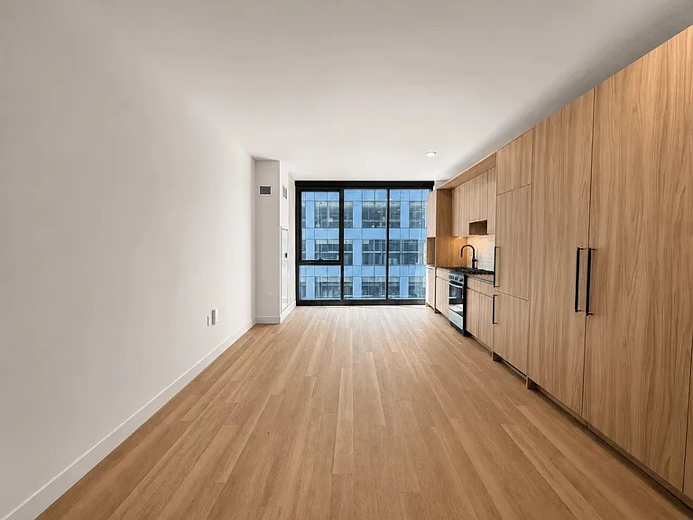 Open-concept studio layout at Stead 220 in Fulton Market featuring 8' Italian wardrobe closets aligned with the kitchen millwork, a full-sized kitchen, and floor-to-ceiling windows with skyline views.
