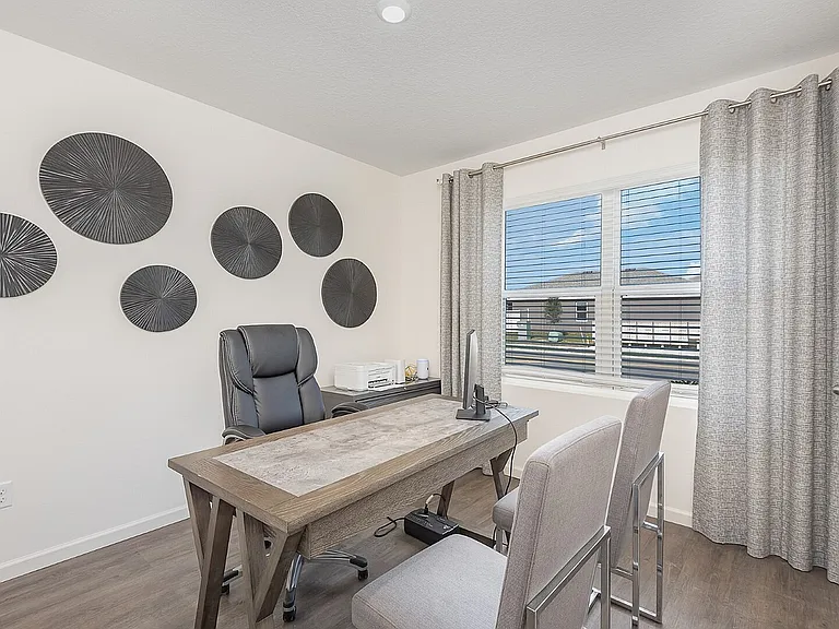 Bright and inviting home office with modern decor, featuring a sleek wooden desk and comfortable seating, complemented by stylish wall accents and a large window with a scenic view.