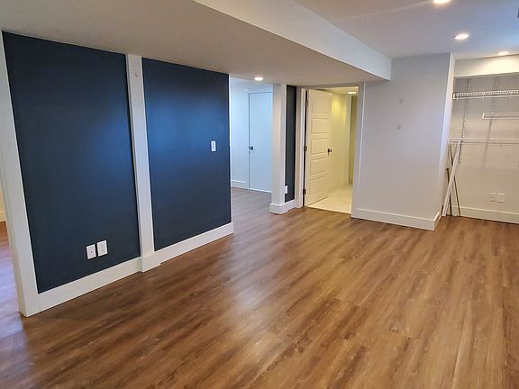 Living room standing at entrance door. First bedroom on left. Bathroom straight ahead on right with kitchen left of that. Living room windows face west.