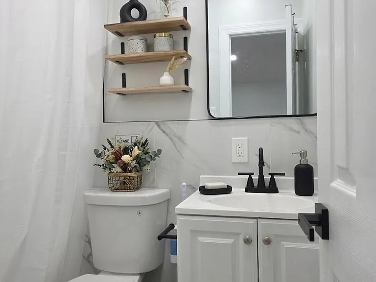 Full bathroom with a single-sink vanity, wall mirror, and open shelving for toiletries, plus a tub/shower combo.