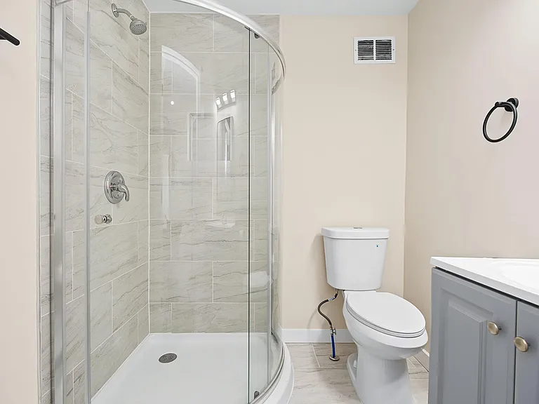 Updated bathroom with a glass-enclosed corner shower, tiled walls, and a vanity with storage for daily essentials.