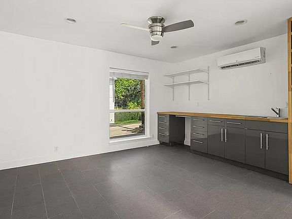 Studio living area. Electric countertop range and compact fridge will be installed prior to move-in. Wardrobe and murphy can also be added by owner. Note small dishwasher and microwave in shelving.