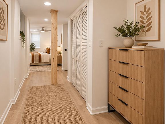Well-lit hallway with wood-look flooring, louvered closet storage, and convenient access to the furnished bedroom.