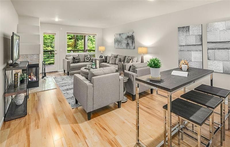Spacious living room with a wood-burning fireplace and connected to a covered patio overlooking wooded area.